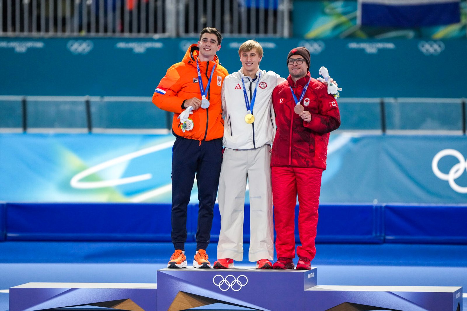 Jenning de Boo, Jordan Stolz en Laurent Dubreuil op het podium na de 500 meter mannen op de Olympische Spelen van 2026